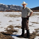 Deputy Refuge Manager Cortez Rohr in a field of melting snow under blue skies with mountains in the background.