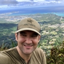 Headshot photo of John Weber atop a mountain in Hawaii with the Mokulua islets and Bellows Air Force Station in the background by John Weber/USFWS.