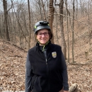 Service employee wearing long sleeves, vest, and caving helmet, smiles at camera 