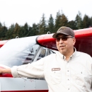 Man in USFWS uniform stands with one hand on the nose of a small red and white plane