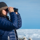 Woman in warm clothing looking out to the snow covered ice with binoculars