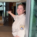 Woman holding door opens extends her arm inviting visitor into the visitor center.