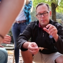 Male biologist kneeling on the ground with attention focused on a small insect on his thumb