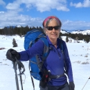 A woman standing in a field of snow with a backpack on and ski poles in her hand