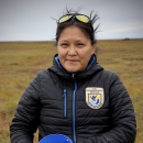 Melissa Brown standing on the tundra, holding a blue bucket partly filled with wild cranberries