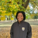 Shanice smiles with hands in pockets. She is wearing a black FWS zip up jacket. 