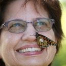 Close-up of a smiling woman with a tagged monarch butterfly on her nose.