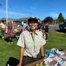 USFWS Staff Karen Ceballos wearing a USFWS official uniform and standing at a craft table at an outdoor festival.