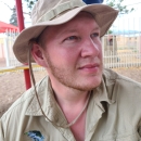 A man wearing a tan jungle hat and collared shirt, with a playground in the background.