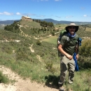 A man stops for a photo while hiking through green rolling hills.