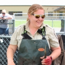 Smiling woman in sunglasses, waders, and Service uniform short-sleeved shirt holds a fish by the tail with a gloved hand.