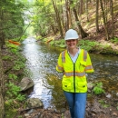 woman in high visibility vest and construction hat in front of stream