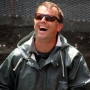 A laughing man in sunglasses and rainjacket stands up to his waist in water in a concrete tank.