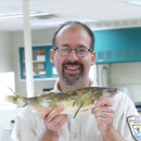 Man smiles whie holding up fish in a lab