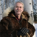 Man in fur parka, with winter birch tree forest in the background