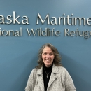 Woman stands in front of Alaska Maritime National Wildlife Refuge written in silver letters on a blue wall.