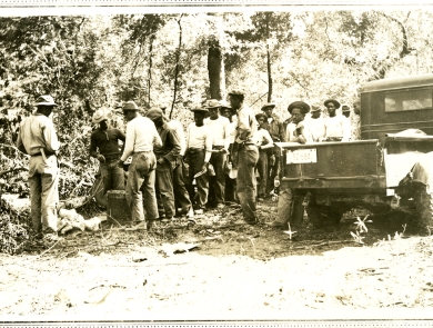 Black and white photo of around 20 African American men in a line in the woods.