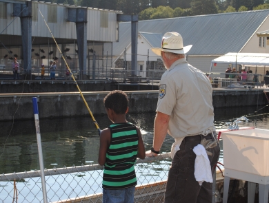 An adult showing a child how to fish looking over the railing at a fish hatchery.