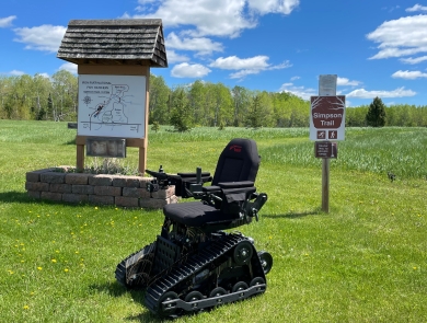 A tracked wheelchair in front of the Simpson Trail sign at Iron River National Fish Hatchery in Wisconsin.