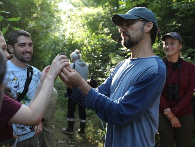 Biologist holds a small songbird up for a group of onlooking students