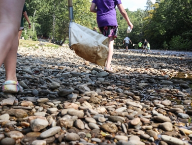 Students walking across a broad, rocky beach to a shallow river