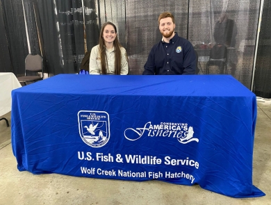 USFWS employee and volunteer sitting behind blue information booth