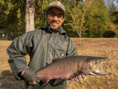 Intern Eric Klingberg poses holding a adult coho salmon at the Quilcene National Fish Hatchery in Quilcene Washington.