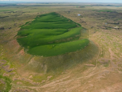 Crops of wheat growing on the top of a flood-carved mesa are a green contrast to the surrounding drier landscape.