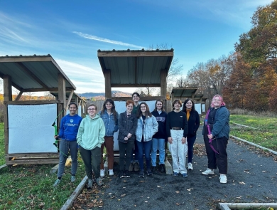 Ten students from Mt. Holyoke stand in front of targets at the Fort River Archery Range.