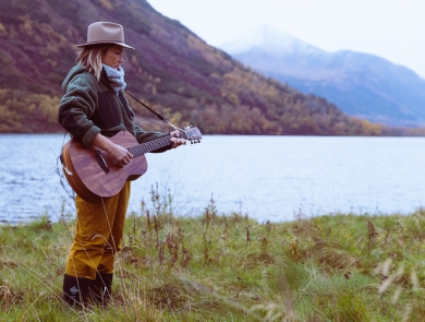 A woman playing guitar next to a lake
