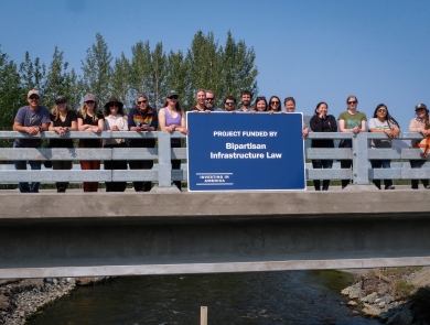 a group of people standing on a bridge over water holding a blue sign