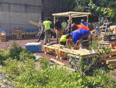 people in colored shirts work in a gravel lot building wooden structures