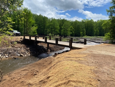 A bridge over a free-flowing creek with burlap covered soil for replanting on the banks