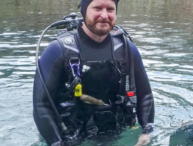 Justin Crow in dive gear, standing in a river. 