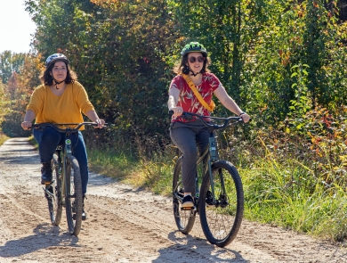 Two woman in bright clothing and helmets riding down a dirt road on electric assisted mountain bikes