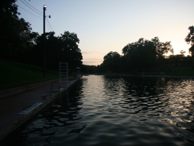 Barton Springs pool is shown against a background of a sunset.