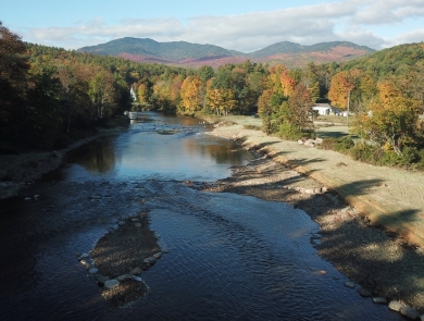 An aerial view of a river surrounded by trees with fall foliage