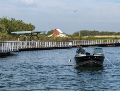 Looking straight at a fishing boat catching a white bass with fishing pier along left side and visitor center in background on a sunny day