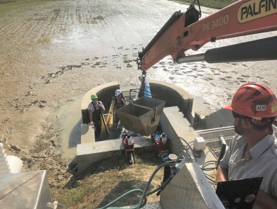 USFWS biologist lowers large bucket using a crane into a newly constructed test kettle in order to move fish out of the pond.