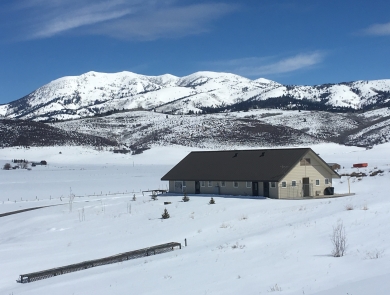 House perched in a snowy meadow, below snow capped mountains. 