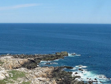 A tall, slender stone lighthouse on a rocky coast of the deep blue ocean