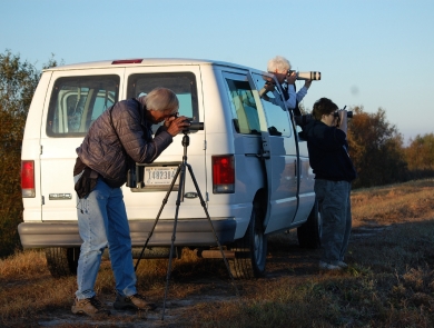 3 people using scopes & binoculars by white van looking for wildlife