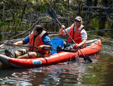 Service intern, Suzena Arias, and employee rafting through wetland to check minnow traps