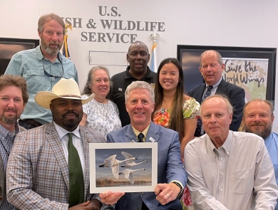 A group of people pose with the winning artwork depicting trumpeter swans.
