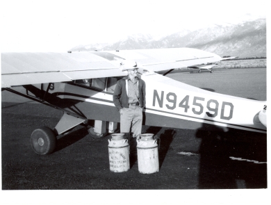 A man stands next to a small aircraft with milk cans of fish to release