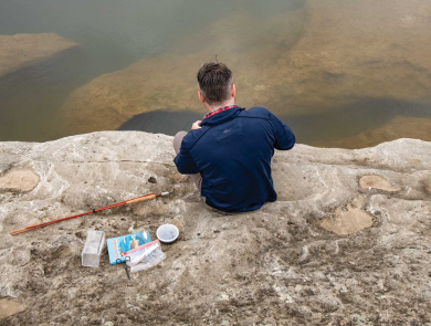 Adam Comer from TPWD sets up microfishing gear on rocky shore. 