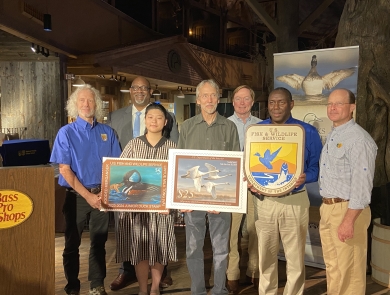 Group photo of people holding duck stamp arts and USFWS logo.