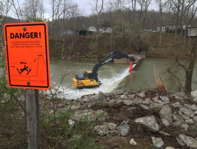 Crane removing dam with danger sign in the foreground
