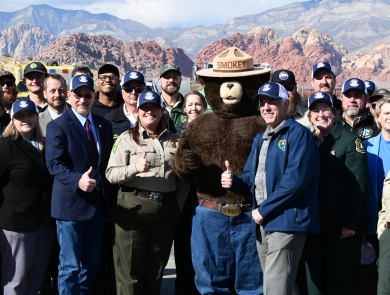 A group of uniformed officials pose with a Smokey mascot