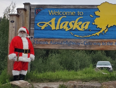 Watercraft inspector, Steve Wogtech, posed in Santa suit in front of Welcome to Alaska sign.